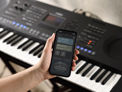 Das PSR-SX620 und eine Hand, die ein Smartphone mit der Anzeige der offiziellen Yamaha-App „Expansion Explorer“ hält.