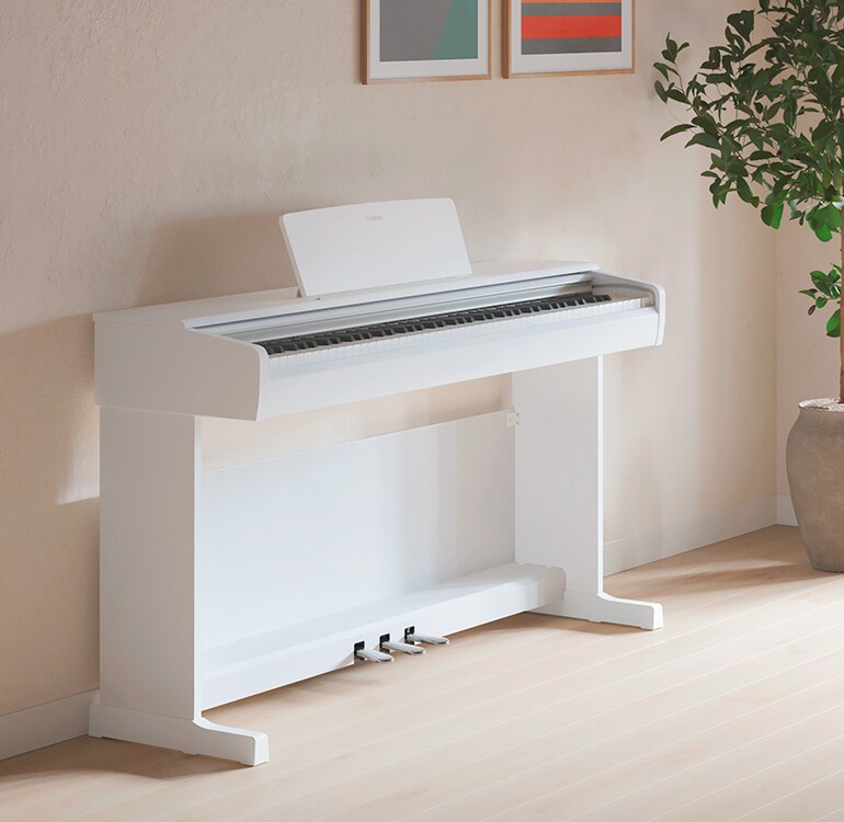 Ein Wohnzimmer mit einem weißen ARIUS Piano, Zimmerpflanzen und einem Sofa, harmonisch in die Einrichtung integriert