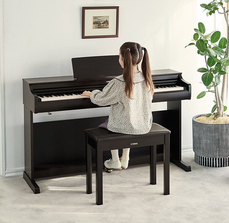 Ein junges Mädchen beim Üben an einem ARIUS Piano in einem Wohnzimmer